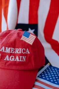 Red cap with 'America Again' text over USA flag backdrop, symbolizing patriotism.