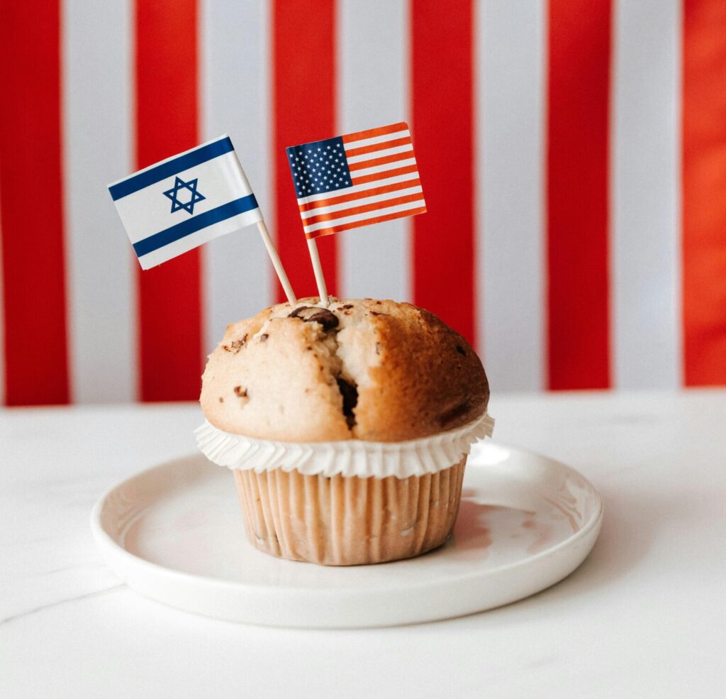 A muffin with American and Israeli flags against USA flag backdrop, symbolizing international relations.