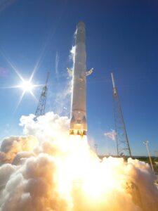 A powerful rocket takes off into a clear blue sky, surrounded by clouds of smoke.