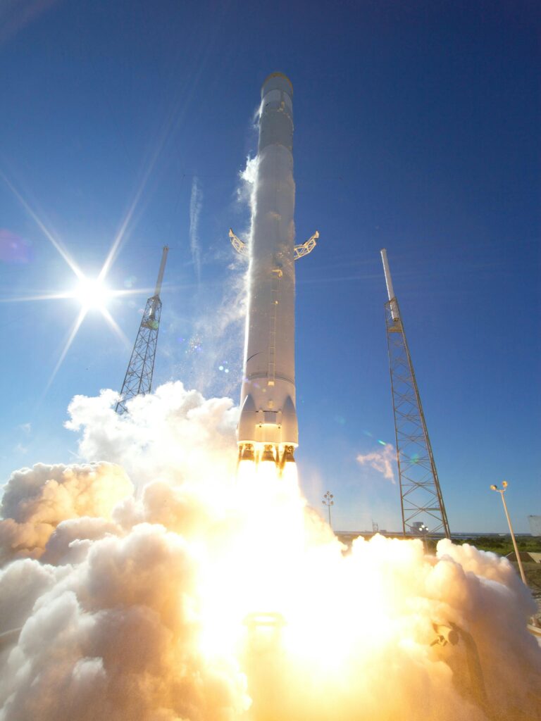 A powerful rocket takes off into a clear blue sky, surrounded by clouds of smoke.